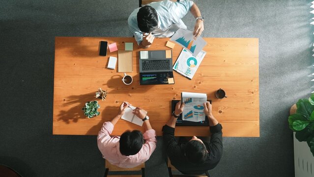 Top aerial view of caucasian business people sharing idea and writing report. Professional diverse people working together and brainstorming marketing plan at meeting table with graph. Convocation.
