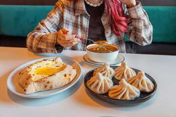 Woman having an authentic Georgian meal with a bowl of Kharcho soup, cheese bread khachapuri, and meat dumplings khinkali