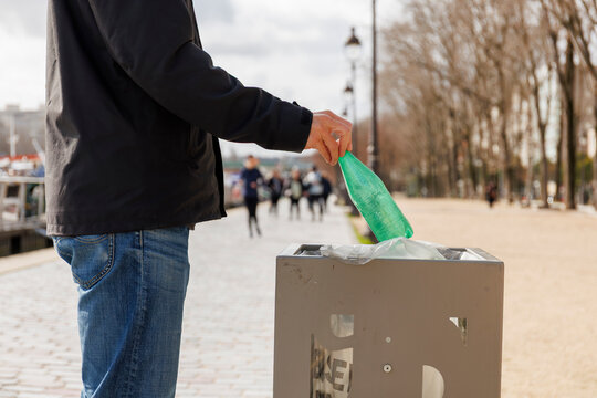 Un homme jette une bouteille plastique dans une poubelle en ville