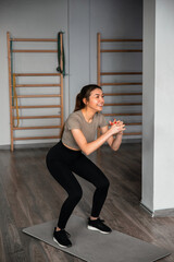 Fototapeta premium Fitness training session in gym with woman doing squats on exercise mat in morning light