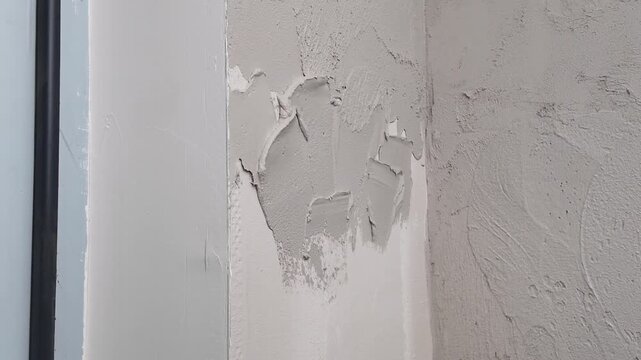 A professional is working on a wall repair in a home. The wall shows damage that needs attention. The plaster is applied carefully to fix the surface.