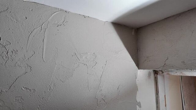 A person applies plaster to the corner of an interior wall in a house. The work is done during the day. The area has good lighting for the task.