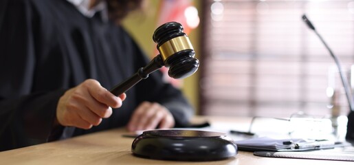 Judge striking gavel at wooden desk indoors, closeup
