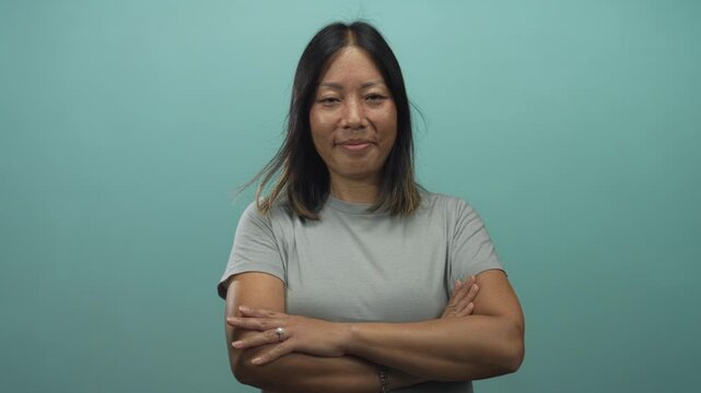 Woman with crossed arms showing ring and bare forearms in studio against teal wall; quiet confidence.