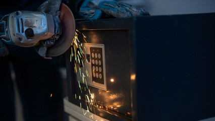 A man breaks into a safe with a grinder.