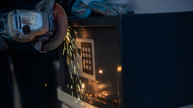 A man breaks into a safe with a grinder.