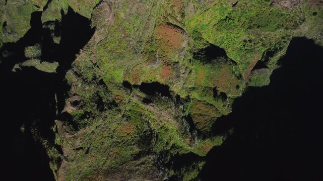 Aerial top down view of rugged volcanic cliffs at Pico do Areeiro. Drone flying sideways over red basalt ridges and green textures in abstract mountain landscape above the clouds in Madeira.