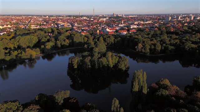 Luftbild Kleinhesseloher See im Englischen Garten, Munchen. Kuenstlicher See mit Inseln, umgeben von Baeumen, Wiesen und Biergarten. Beliebter Ort fuer Erholung und Reisen.
