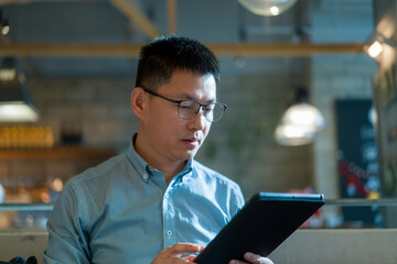 A young man wearing glasses focuses intently on using a tablet computer indoors