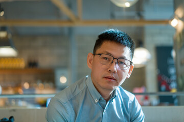 Obraz premium Middle-aged Asian man wearing glasses looking directly at the camera in an indoor setting