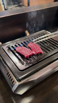 Delicious slices of premium marbled Wagyu beef sizzling on a hot tabletop grill. Japanese yakiniku style of cooking fresh, fatty meat