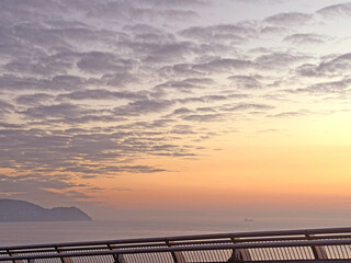 Fototapeta premium Serene sunrise over the ocean with textured clouds and distant coastline view