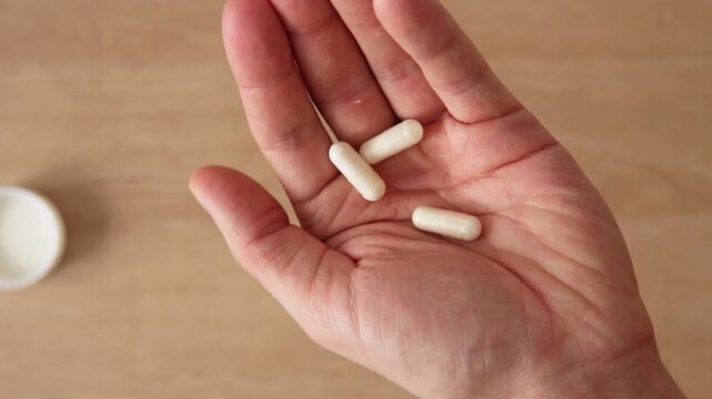 op view of man pouring white vitamin capsules into his open palm from plastic white bottle in slow motion for daily health supplement and medical wellness routine