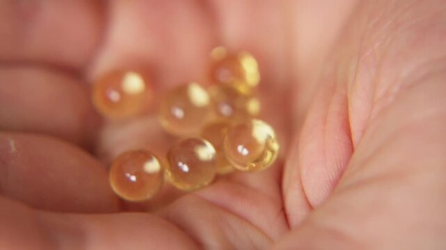 close up of man pouring yellow omega three fish oil capsules into his open palm while standing in modern kitchen at home for daily healthy lifestyle routine