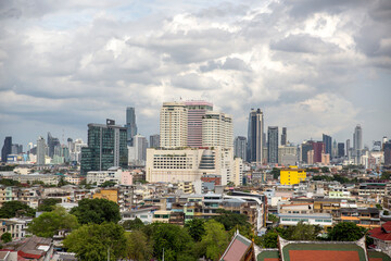 Fototapeta premium Panorama of the Bangkok skyline. Dense mix of high-rise buildings and modern skyscrapers, including several prominent hotels and commercial towers, under a overcast sky filled with soft grey clouds.