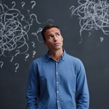 Pensive young caucasian male contemplating solutions with question marks on chalkboard