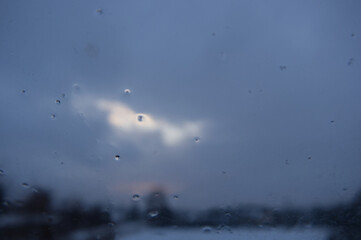 Raindrops on window glass with blurred clouds and sky in the background after a winter storm.