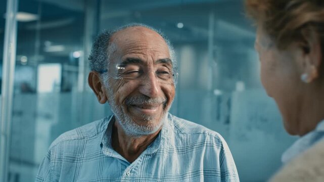 Woman adjusts smart glasses on senior man. Futuristic transparent eyewear tried on. Elderly couple explores wearable technology. Modern office with glass walls. He looks at her warmly.