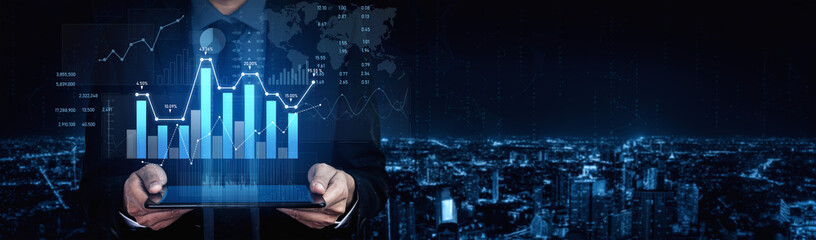 A businessman stands against a city skyline at night, holding a tablet that displays advanced financial data and charts, symbolizing innovation in business analytics. Scalp © InfiniteFlow