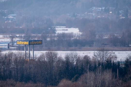 Polska, Ostrowiec Świętokrzyski, 2 lutego 2026, 13:55. Szyld Castoramy na betonowych palach , market budowlany, w mglisty, zimowy dzień. Wok&oacute;ł szyldu rosną bezlistne drzewa, typowe dla zimy, z łatami 