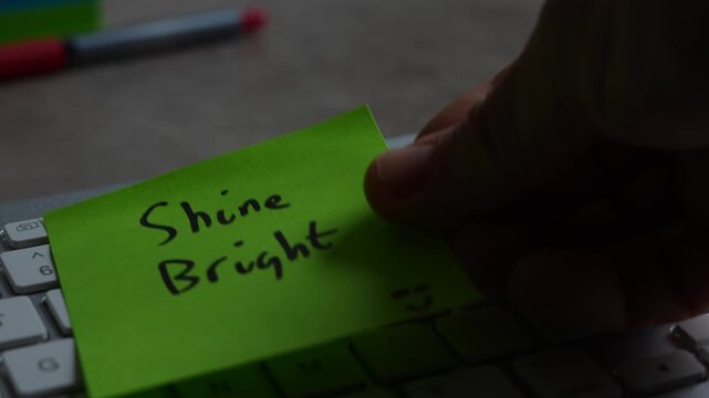 "Shine Bright" green sticky note left on keyboard. The bright note stands out against the keys, symbolising motivation, productivity, and a focused mindset. Shot in 4K, slow-motion, 50FPS.