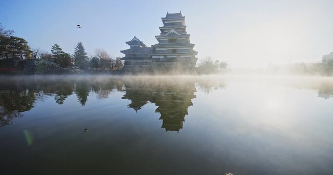 Cinematic reflection of beautiful 16th century Matsumoto castle in misty pond at sunrise