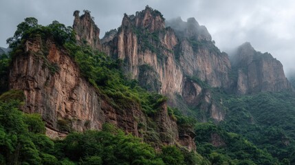 Fototapeta premium Steep cliffs tower above the lush green trees. Dark clouds gather around the mountain peaks. This scene shows the wilderness in a remote region on a cloudy day.