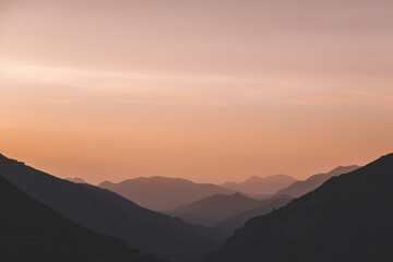 Fototapeta premium Minimalistic mountain landscape at sunset with layered silhouettes of hills fading into soft orange sky, tranquil evening atmosphere, concept serenity, meditation, travel inspiration natural beauty