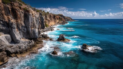 Obraz premium Waves crash against a rocky shoreline under a clear sky. The water is a vibrant blue with white foam. This coastal scene shows the beauty of nature by the sea.