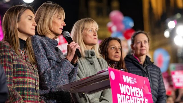 Group of diverse women speaking at a rally for women's rights, with a microphone and colorful balloons in the background, advocating for equality and justice