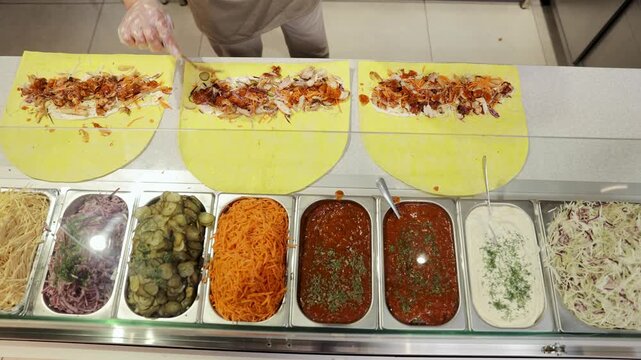 Chef assembling a classic shawarma with grilled chicken, pickled cucumbers, carrots, and cabbage on a yellow pita bread
