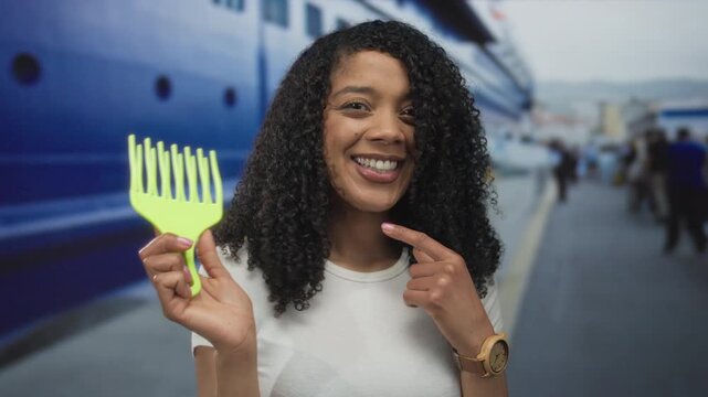 African american woman with curly hair holds bright green pick comb and points finger to comb on street; confidence.