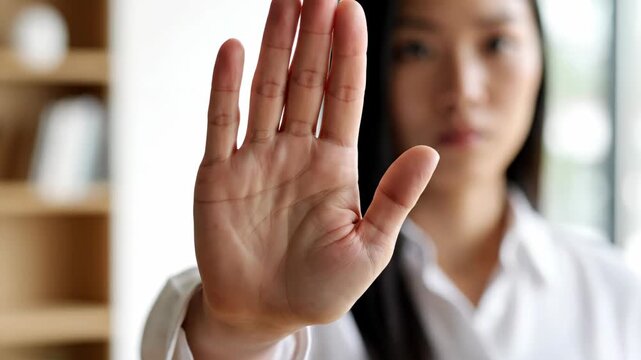 Serious Asian woman showing stop gesture with open palm
