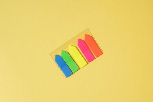 Minimalist flat lay of colorful neon sticky index tabs on a solid yellow background. Top-down view with copy space. For office, school, organization, and creative concepts.