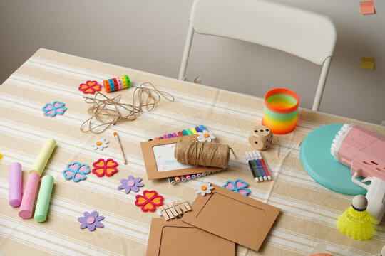 A child's messy activity table with colorful arts and crafts supplies and various toys. A scene of creative playtime, DIY projects, and childhood fun. Natural light on a striped tablecloth.
