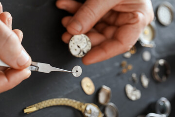 Senior man fixing mechanism of vintage wrist watch at black table, above view