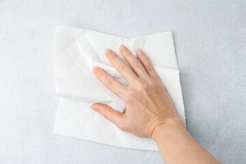 Woman wiping light grey surface with paper towel, top view