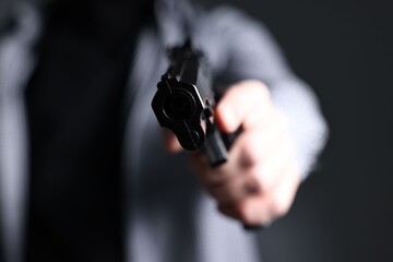 Fototapeta premium Dangerous criminal holding gun on dark grey background, closeup. Armed robbery