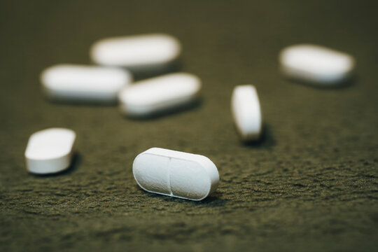 White oblong pills scattered on soft green background, pharmaceutical tablets on herbal surface
