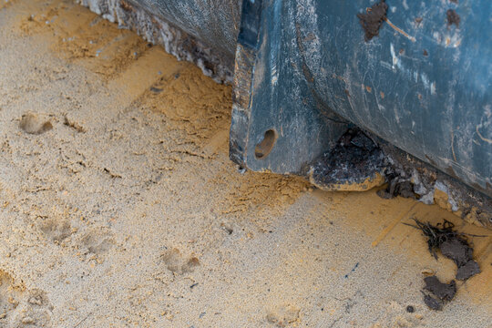 Close-up of animal tracks in smooth sand beside the metal edge of an earthmoving bucket.