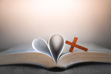 open bible with heart shaped pages and wooden cross, christian love and faith concept
