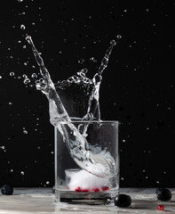 A glass of water with a pomegranate infused ice cube dropped in causing splash.
