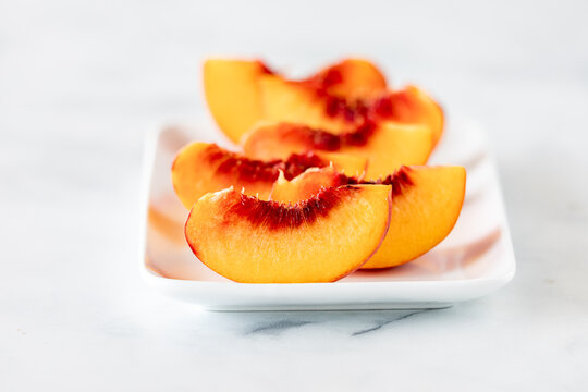 Slices of fresh freestone peaches on a white platter.