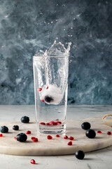 A tall glass of water with a berry infused ice cube dropped in causing a splash.