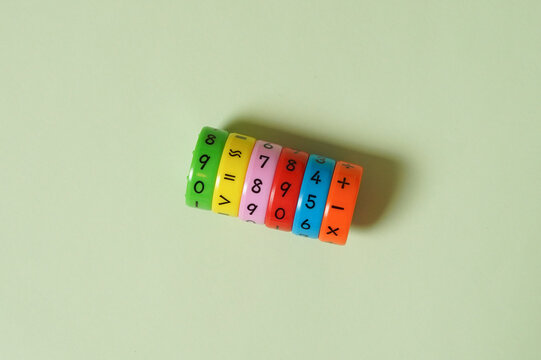 A colorful cylindrical math puzzle with colorful number rings for children's early education. This flat lay shot shows the toy on a minimalist pastel green background. Concept for learning, arithmetic