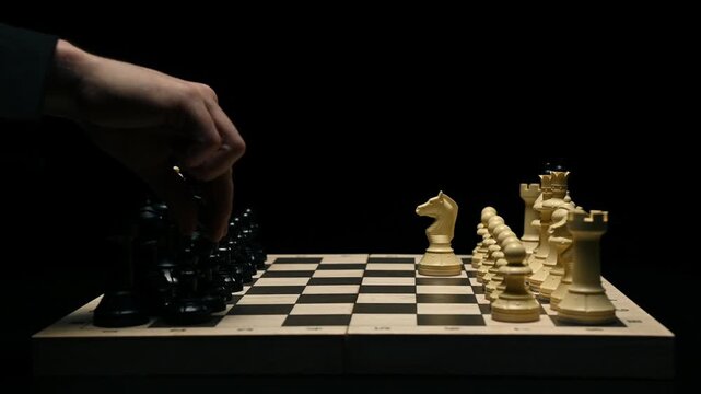 A chess game on a black background. A chess player makes the first move in the game. Close-up of a chess player's hand as they move a pawn and start the match