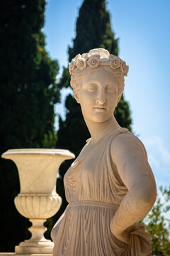 Portrait of a Statue of a Greek mythical Muse in the Achilleion Palace in Corfu, Greece, Cypress Trees and Vase in Background, sunny Day