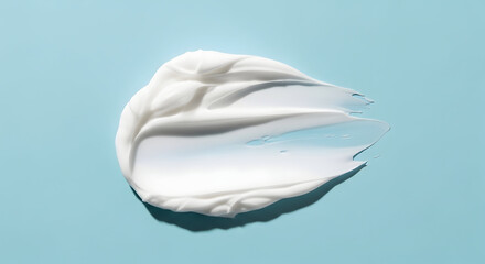 Smoothed out dollop of white cosmetic cream on a pastel blue background, beauty and skincare concept.