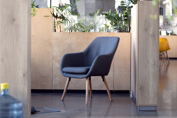 Modern gray armchair with wooden legs in a contemporary office space with plants © Artem Kniaz