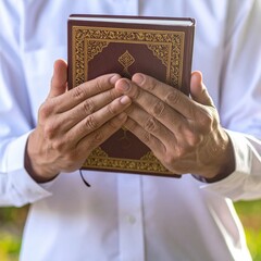 Close Up Of Man Hands Holding An Ornate Burgundy Quran Book With Gold Embossing In Natural Daylight Outdoor Setting